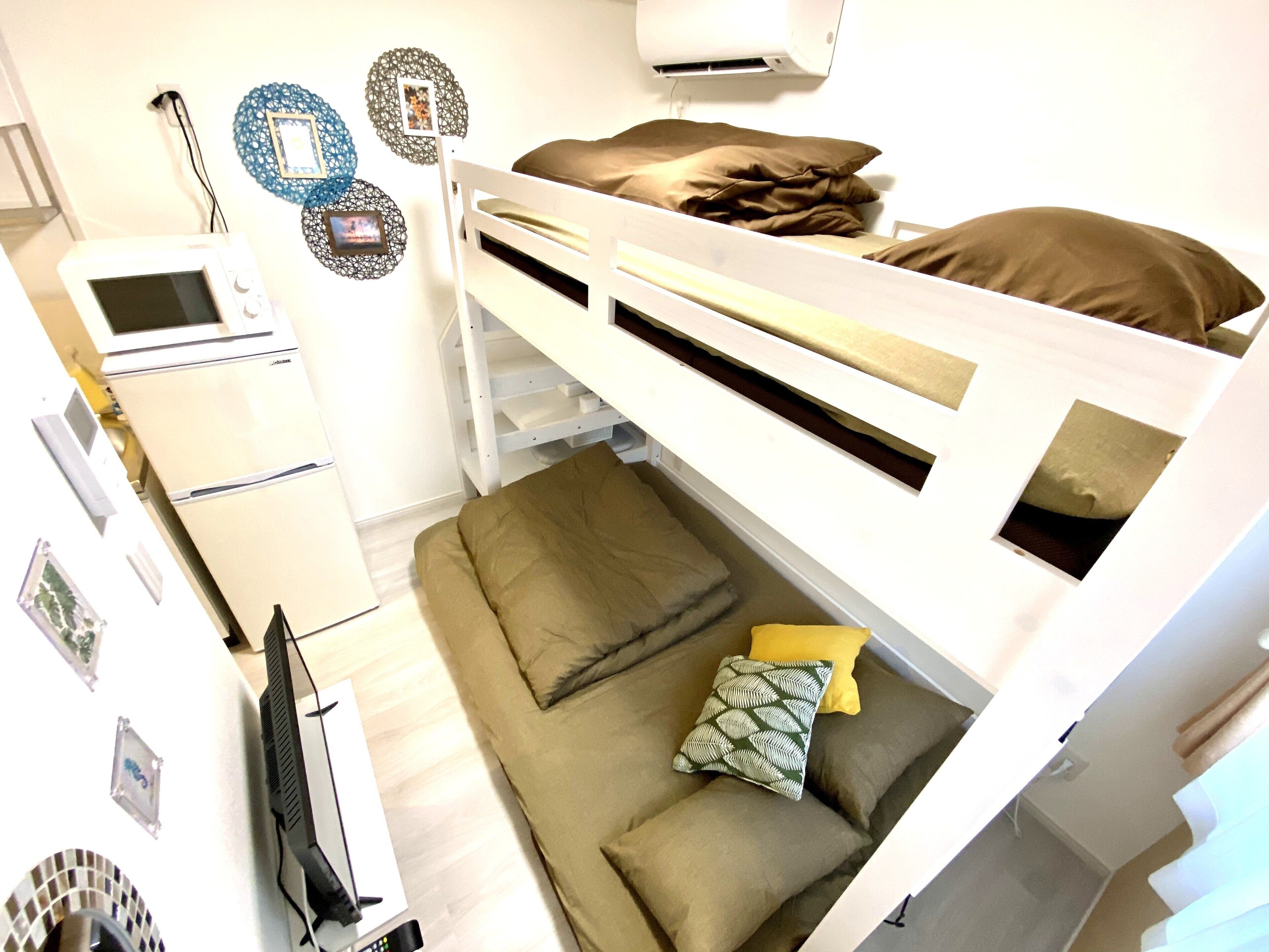 A compact room with a bunk bed, a small kitchenette, and a sofa with cushions.