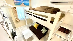A bunk bed room with a small table and a bench, a wall-mounted air conditioner, and a painting of a pier. - Le Soleil Asato (Naha)