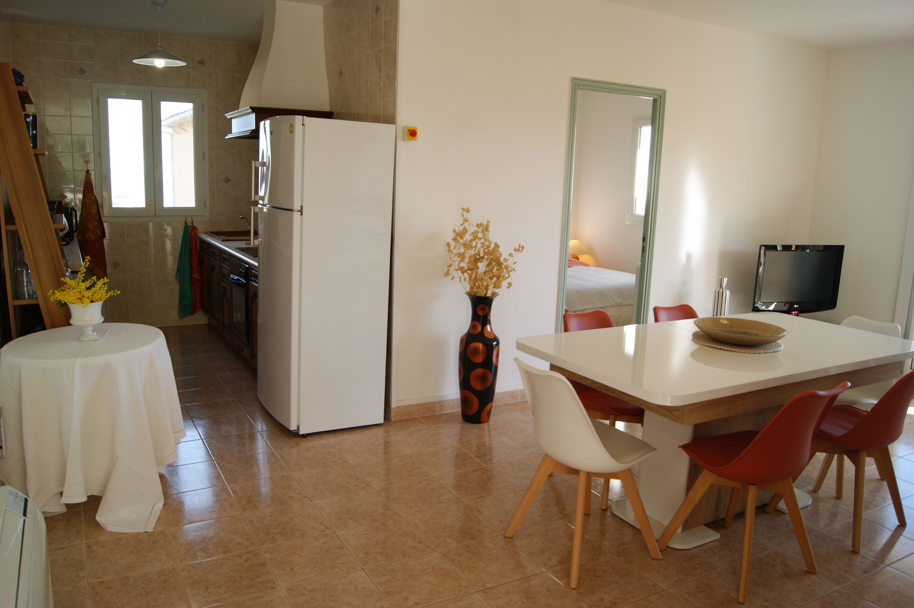 Une cuisine compacte comprenant un réfrigérateur, une table à manger avec des chaises et un vase contenant des fleurs séchées.
