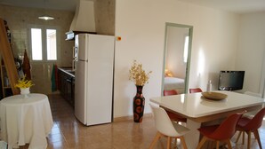 A compact kitchen with a refrigerator, a dining table with chairs, and a vase with dried flowers.