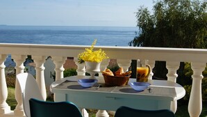 A table set with croissants, a basket, and a glass of orange juice on a balcony overlooking the sea.