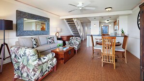 A spacious living room with a sofa, armchairs, a dining table with chairs, a ceiling fan, and a staircase leading to an upper level. - Expansive Views with new split system AC! (Koloa)
