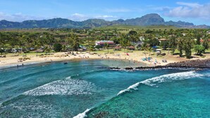 A beach with clear turquoise waters, a sandy shore, and a backdrop of lush green hills and a mountain. - Expansive Views with new split system AC! (Koloa)
