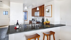 A modern kitchen with a central island, stainless steel appliances, and wooden bar stools. - Expansive Views with new split system AC! (Koloa)