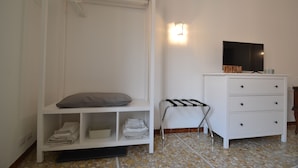 Un dormitori amb un llit, un armari blanc, una taula petita i un televisor fixat a la paret.