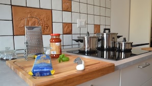 Una cuina amb una taula de tall de fusta, un rallador, un bocal de cafè, un sac de farina, una ampolla de ketchup, un ou blanc i olles d'acer inoxidable damunt la cuina.