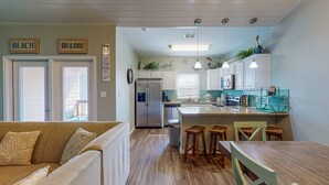 Une cuisine moderne avec des meubles blancs, un réfrigérateur en acier inoxydable et un coin repas comprenant une table en bois et des tabourets de bar.