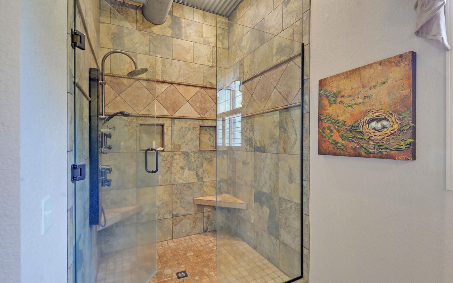 A glass-enclosed shower with a handheld showerhead, a wall-mounted towel rack, and a small shelf.