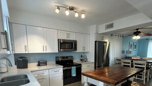 A modern kitchen with white cabinets, stainless steel appliances, and a wooden island with stools. - Paradise awaits! (Sarasota)
