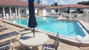 A swimming pool with lounge chairs and umbrellas, surrounded by buildings with red roofs. - Paradise awaits! (Sarasota)