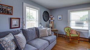 A living room with a grey sofa, a wicker chair, and a framed picture on the wall. - Willoughby 4BR Coastal Home • Steps to Shore (Norfolk)
