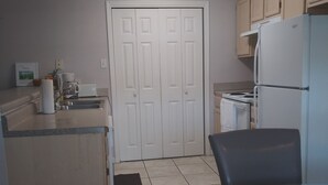Una cocina con un refrigerador blanco, una estufa, un lavamanos y un comedor con una mesa de vidrio y sillas.