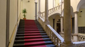 Una imponente escalera con peldaños alternados en rojo y negro, flanqueada por columnas y barandillas blancas, que conduce a un piso superior.