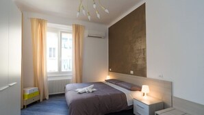 Un dormitorio moderno con una cama grande, lámparas de noche, una ventana con cortinas y un radiador.