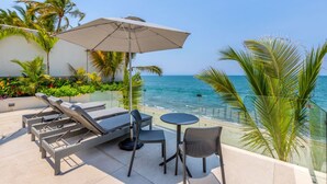 A terrace with lounge chairs, a table, and an umbrella overlooking a beach with palm trees and the ocean. - Luxury 4 bed/4 bath Beach Front Condo - Bucerias (Bucerías)