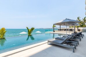 Zona junto a la piscina con sillones de descanso y sombrillas, con vistas al mar.