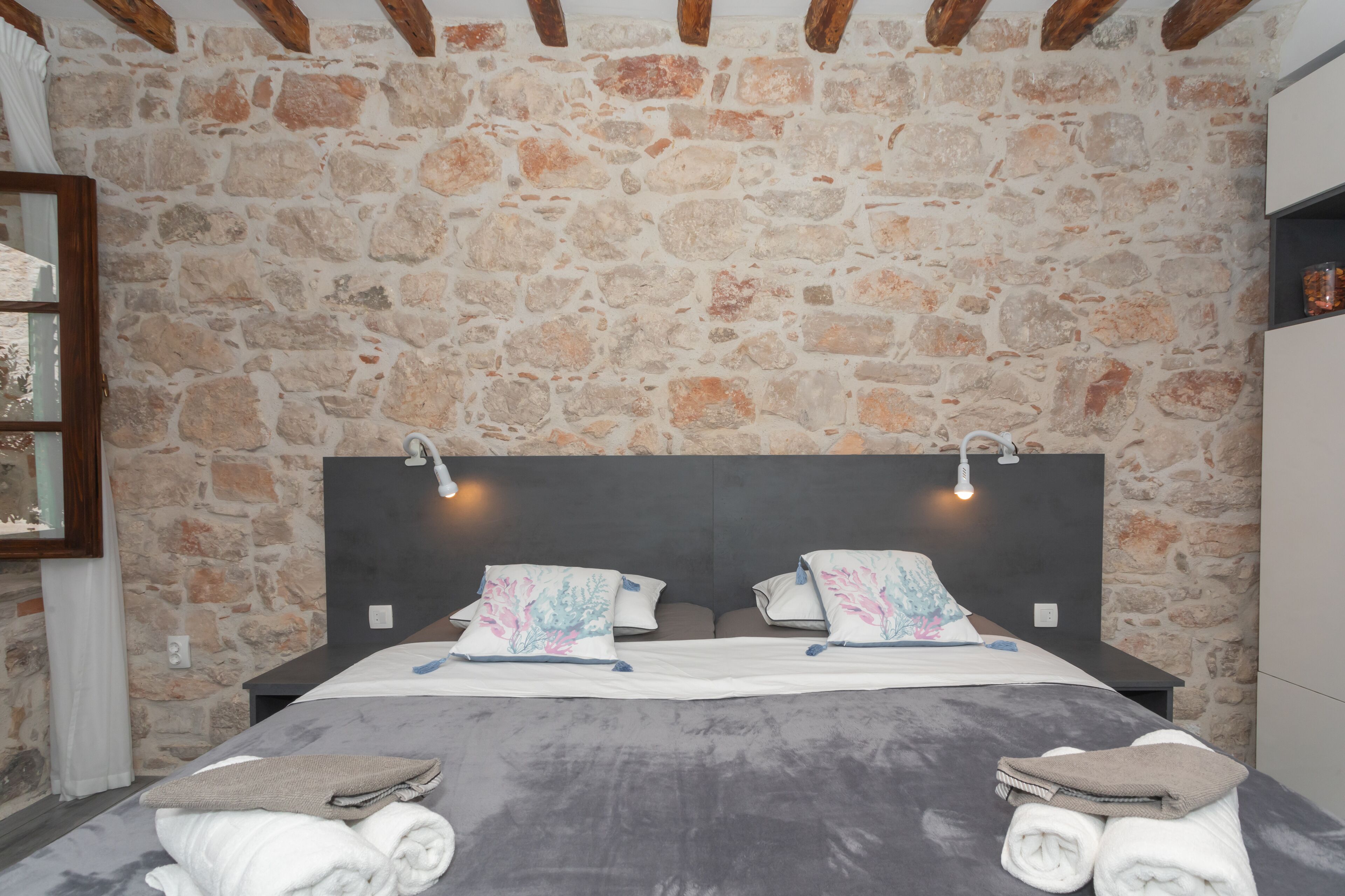 Un dormitorio con pared de piedra, una cama con dos almohadas y un cabecero.