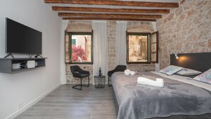 Un dormitorio con una cama, dos sillas, un televisor y una pared de piedra.