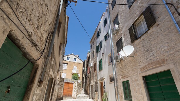 Una calle estrecha con edificios de piedra, una puerta de madera y una antena parabólica.