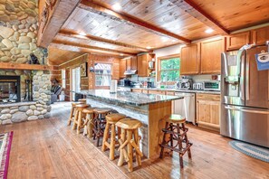 A spacious kitchen with wooden cabinets, a large island with stools, and a stone accent wall. - Sauna & Cold Plunge! Custom-Built Clarklake Cabin (Clarklake)