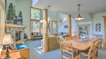 A cozy living room with a stone fireplace, wooden furniture, and a dining area with a table and chairs.