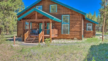 A wooden cabin with a porch, a covered deck, and a small front yard.
