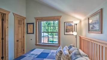 A bedroom with a large bed, wooden headboard, a window with a view of greenery, and a framed picture on the wall.