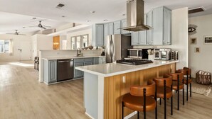 Una cocina moderna con armarios grises, electrodomésticos de acero inoxidable y una isla central con taburetes de bar.