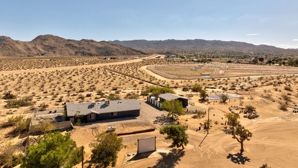 Paisatge de desert amb vegetació escassa, alguns edificis i muntanyes a la distància.