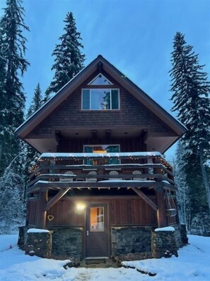 A multi-story wooden cabin with a balcony, surrounded by snow-covered trees. - Bl455 (Whitefish)