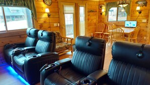 A cabin interior with two massage chairs, a wooden dining table, and a laptop on a desk.