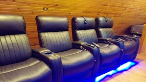 A row of black leather massage chairs with blue LED lighting, wooden panel walls, and a small wooden table with a remote control.