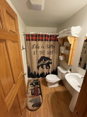Un baño con puerta de madera, inodoro, lavamanos y cortina de ducha con estampado de animales.