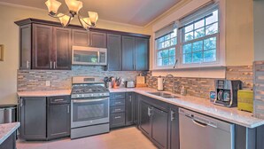 A modern kitchen with dark cabinetry, a stainless steel stove, a microwave, and a dishwasher. There is a window with blinds, a chandelier, and a countertop with a coffee maker. - Cozy Birmingham Abode < 7 Mi to Downtown Fun! (Birmingham)