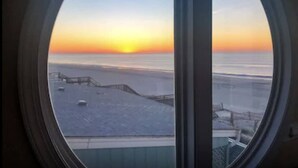 Blick aus einem Fenster mit rundem Rahmen auf eine verschneite Landschaft bei Sonnenuntergang.