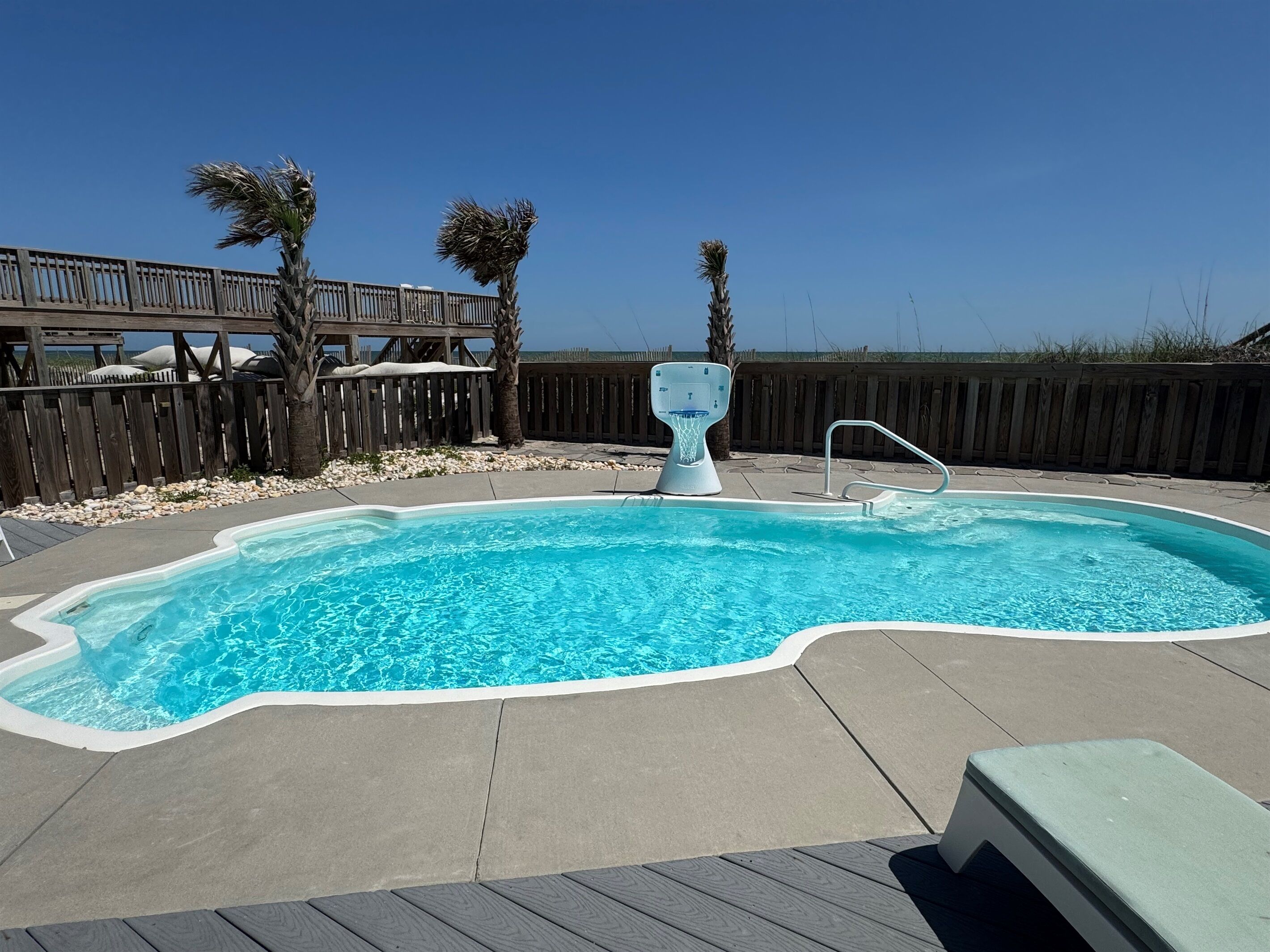 A swimming pool with a wooden deck, a wooden fence, and palm trees.