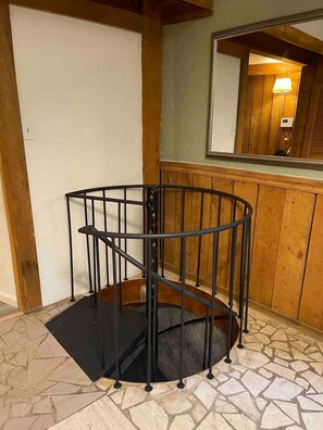Una escalera de caracol con barandilla de metal, paneles de madera en las paredes y suelo de baldosas.