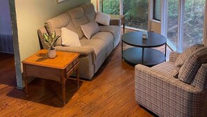 A cozy living room with a sofa, a round coffee table, and a chair. There are two lamps on the side tables, and a ceiling fan above. - TreeTops in Town Private & Peaceful (Charleston)