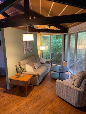 A cozy living room with a sofa, a round coffee table, and a chair. There are two lamps on the side tables, and a ceiling fan above. - TreeTops in Town Private & Peaceful (Charleston)