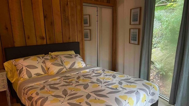 A bedroom with a bed, wooden panel walls, a window with curtains, and framed pictures on the wall. - TreeTops in Town Private & Peaceful (Charleston)