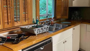 A kitchen with wooden cabinets, a dishwasher, and a window with a view of greenery. - TreeTops in Town Private & Peaceful (Charleston)