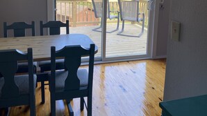 Een kamer met een houten eettafel en stoelen, een schuifdeur naar een terras met een houten hekwerk.