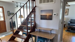 Una escalera de madera con peldaños que conducen a un segundo piso, una mesa de comedor con sillas y una sala de estar con un sofá y una mesita de centro.