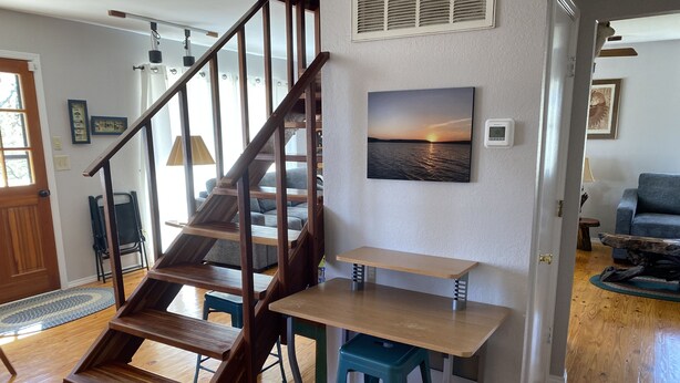 Een trap met houten treden die leidt naar een tweede verdieping, een eettafel met stoelen en een zithoek met een bank en een salontafel.