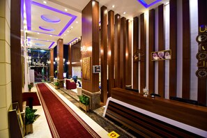 A hotel lobby with a red carpet, wooden paneling, and a reception desk. - Laylati Al Hamra (Riyadh)