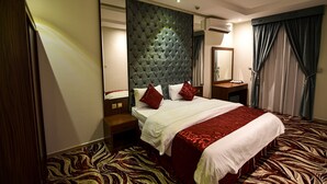 Habitación de hotel con una cama grande, cabecera capitonada, espejo, mesita de noche y alfombra con estampado de cebra.