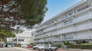 Un edificio a più piani con balconi, un ristorante e un'area parcheggio con diverse auto.