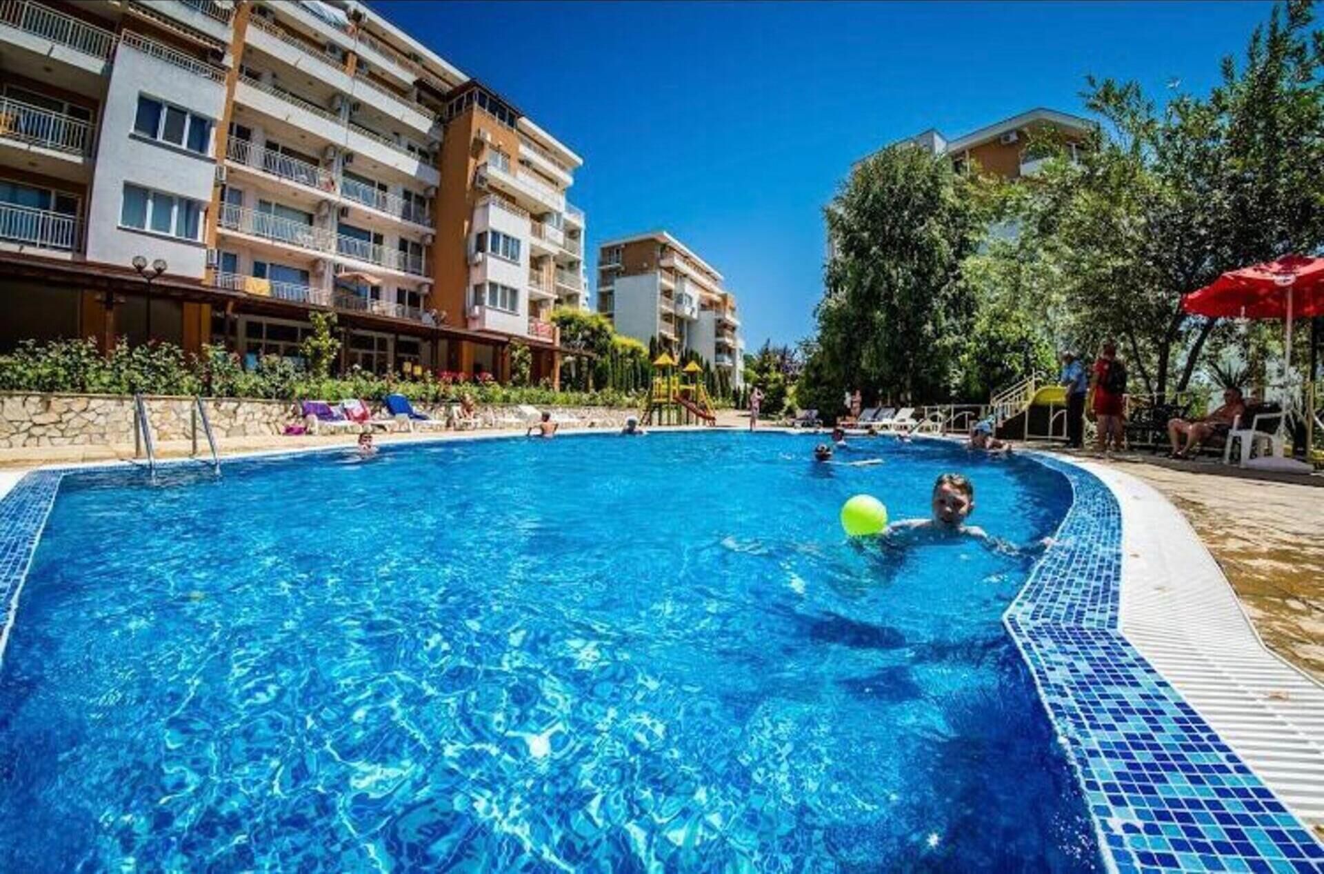 A swimming pool with clear blue water, surrounded by a stone wall and a row of lounge chairs.