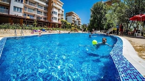 En swimmingpool med kristallklart blått vatten, omgiven av en stenmur och en rad solstolar.