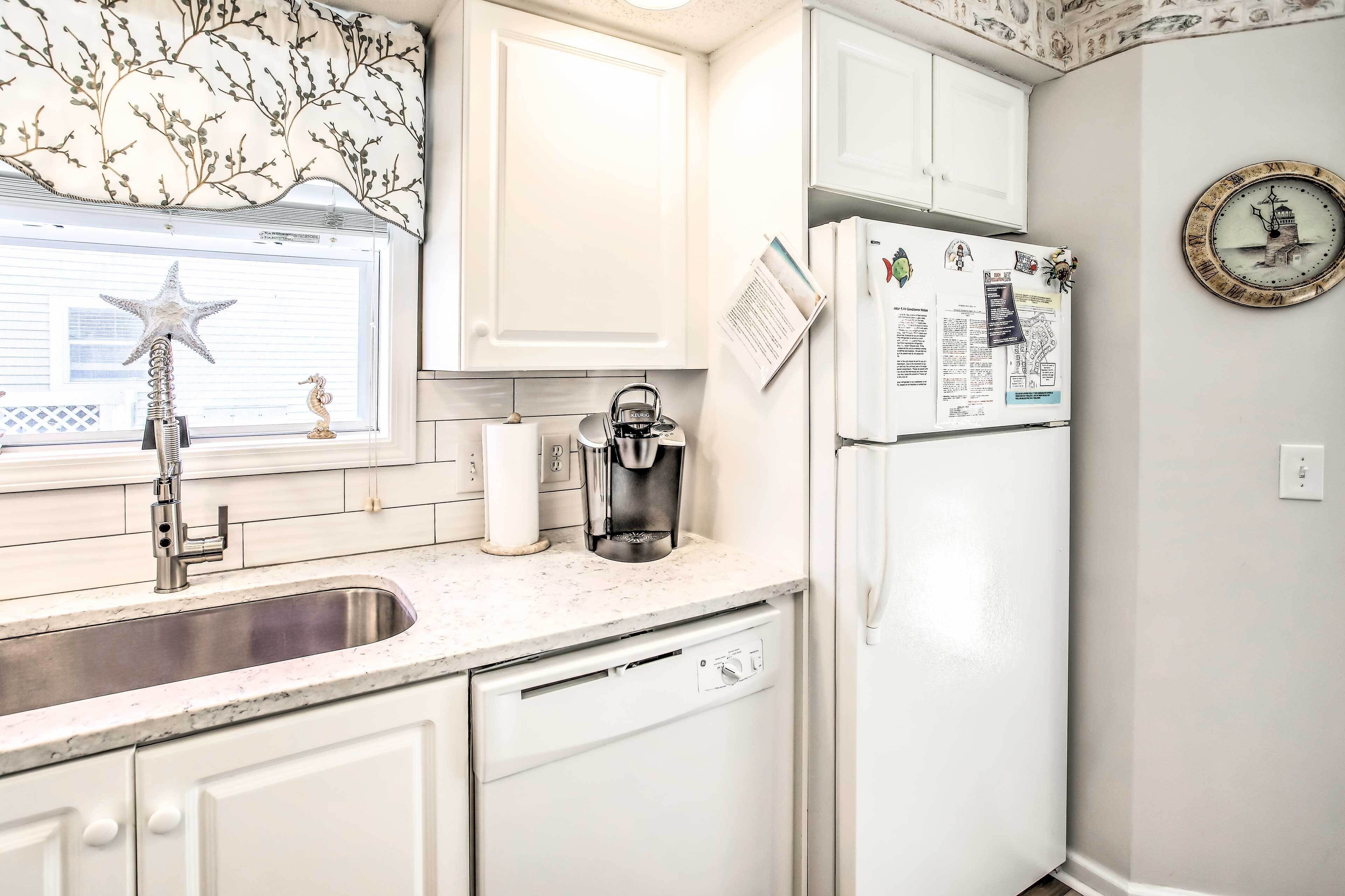 A modern kitchen with white cabinetry, a stainless steel sink, a coffee maker, and a refrigerator with magnets and notes.